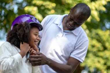 Aile zamanı. Koyu tenli bir adam çocuğunun koruyucu etek giymesine yardım ediyor.