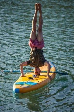 Nehirdeki SUP panosunda yoga yapan bir adam, amuda kalkıyor..