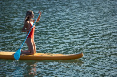 Sağlıklı yaşam tarzı, su sporları. Okyanusta yüzen sörf tahtasında kürek çeken bir kız..