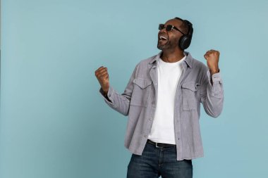 Son derece mutlu bir adam canlı müzik dinler modern stereo kulaklıklar, yumruklarını mavi arka planda saklar.
