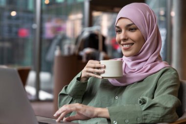 Dijital göçebe. Kafede çalışan ve memnun görünen tesettürlü genç bir kadın.