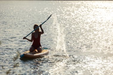 Gün batımında denizde kürek çeken güzel bir kadın.