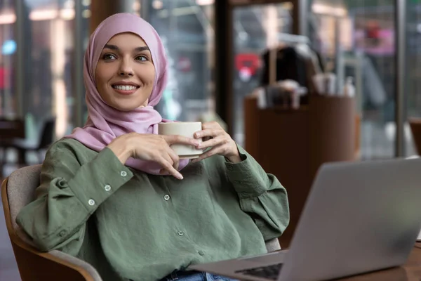 Digital nomad. Young woman in hijab working in a cafe and looking contented