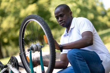 Bisiklet tamir ediyorum. Koyu tenli adam parkta bisiklet tamir ediyor.