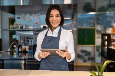 Kahve dükkanı. Elinde tabletle gülümseyen hoş, koyu renk saçlı bir kahve dükkanı asistanı.