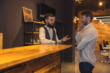 Berber dükkanında kuaförle konuşan genç bir müşteri..