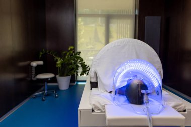 LED lambanın altında uzanan koruyucu gözlüklü kadın güzellik salonunda renkli ışık terapisi görüyor..
