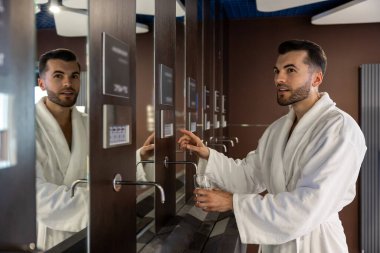 Beyaz bornozlu yakışıklı beyaz adam güzellik salonunda su arıtma kursu içiyor..