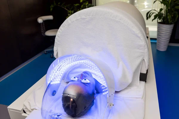 Kobieta Okularach Ochronnych Leżących Pod Lampą Led Kolorowej Terapii Światłem — Zdjęcie stockowe