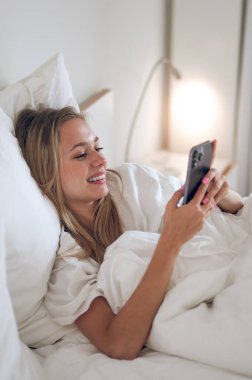 Bağlandı. Genç kız yatakta uzanıyor ve elinde bir akıllı telefon tutuyor.