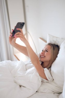 Bağlandı. Genç kız yatakta uzanıyor ve elinde bir akıllı telefon tutuyor.