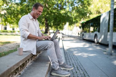 Şehir parkında dizüstü bilgisayarda çalışan orta yaşlı serbest programcının yan görüntüsü.
