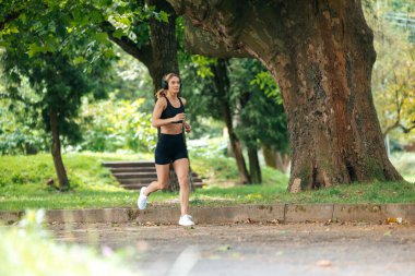 Doğada koşmak. Yaz antrenmanı. Formda ve güçlü. Atletik güçlü sarışın koşucu kulaklıklı kadın parkta koşuyor..
