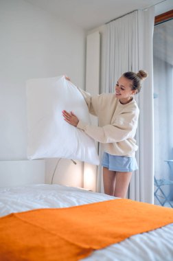 Evde sabahlar. Beyazlı kız sabah yatağını yapıyor.