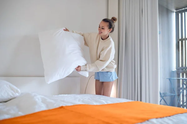 Morning at home. Girl in white making bed in the morning
