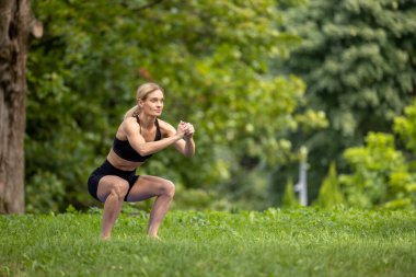 Fitness yaşam tarzı. Park eğitimi. Sağlıklı bir yaz. Güzel bir kadın yaz parkında çömelme egzersizi yapıyor..