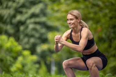 Güzel vücut. Çömelme hareketi. Formda ve aktif. Güzel bir kadın yaz parkında çömelme egzersizi yapıyor..