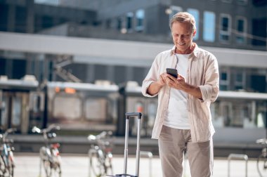 Gülümseyen orta yaşlı adam şehir caddesinde cep telefonu kullanıyor..