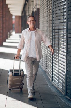 Gülümseyen tatmin olmuş bir adam valiziyle şehirde yürüyor..