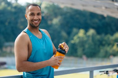 Sporcu. Elinde bardak olmadan gülümseyen yakışıklı sporcu.