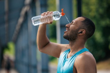 Antrenmandan sonra. Genç esmer tenli sporcu idmandan sonra üzerine biraz serinletici su döktü.
