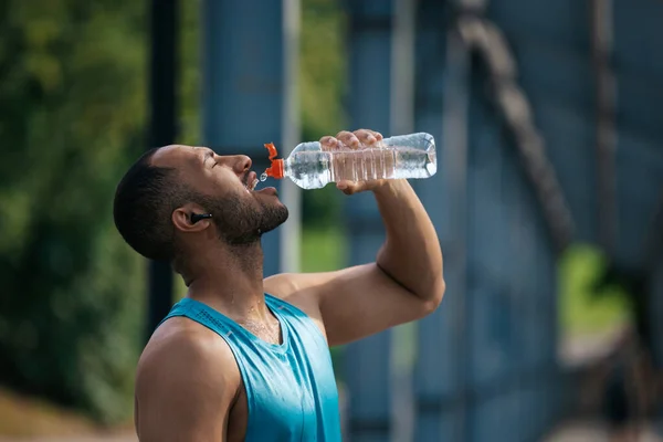 After workout. Well-built handsome sportsman drinking water after workout