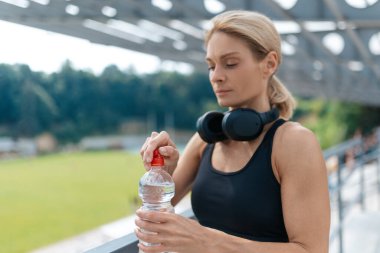 Koştuktan sonra plastik şişeden su içen atletik kadın, dışarıda antreman yaptıktan sonra dinleniyor..