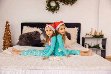 Noel şapkalı sevimli ikizler yatakta oynuyorlar.