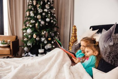 Yatakta uzanmış peri masalları okuyan iki tatlı kız.