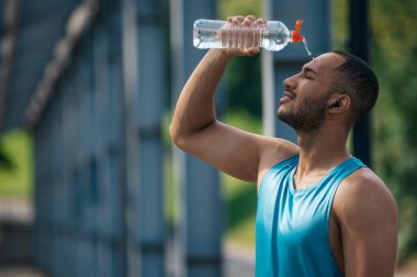 Antrenmandan sonra. Genç esmer tenli sporcu idmandan sonra üzerine biraz serinletici su döktü.