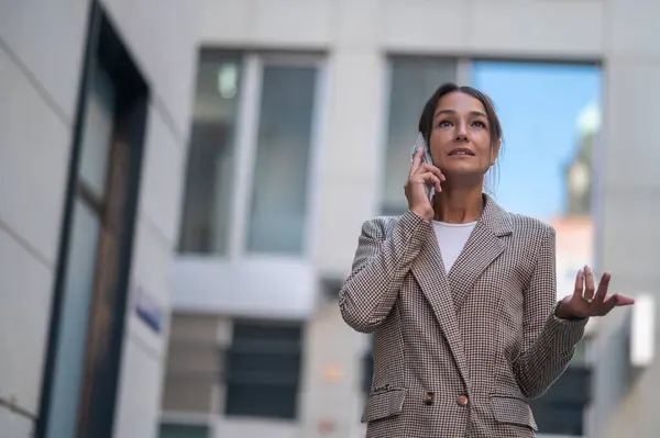 Adult successful businesswoman leader wearing suit standing in city talking on mobile phone.