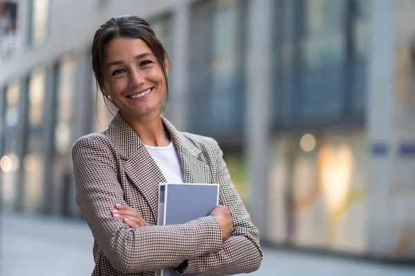Wanita Bisnis Tersenyum Mengenakan Jaket Krem Merangkul Buku Sementara Berpose — Stok Foto