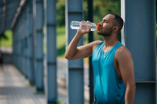 After workout. Well-built handsome sportsman drinking water after workout