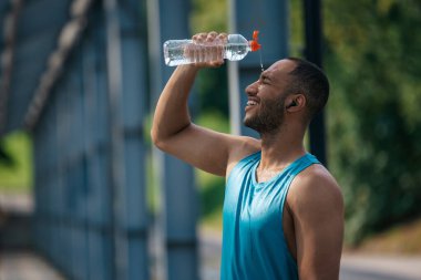 Antrenmandan sonra. Genç esmer tenli sporcu idmandan sonra üzerine biraz serinletici su döktü.