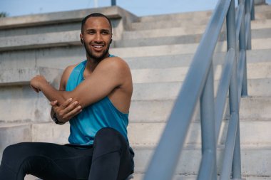 Egzersiz yapıyorum. Koyu tenli sporcu kollarını uzatıyor ve mutlu görünüyor.