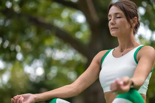 Meditation. Woman in green sportswear sitting in a lotus pose and meditating