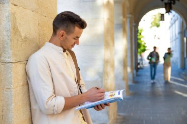 Öğrenci. Duvarın yanında elinde kitapla duran yakışıklı genç adam.
