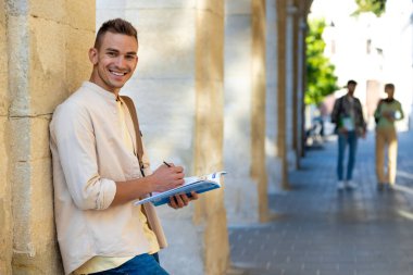 Öğrenci. Duvarın yanında elinde kitapla duran yakışıklı genç adam.