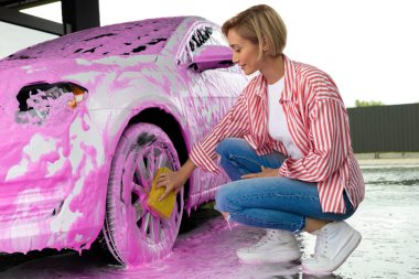 Arabayı temizliyorum. Sarışın kadın renkli bir köpükle arabayı yıkıyor.