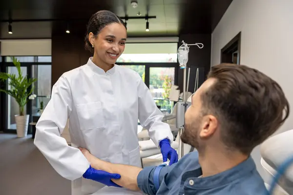診療所のドリップの挿入のための男性の顧客の腕を準備する医師の化粧品学者 — ストック写真