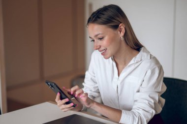 İş yerinde. Beyaz bluzlu, elinde telefon olan hoş bir iş kadını.