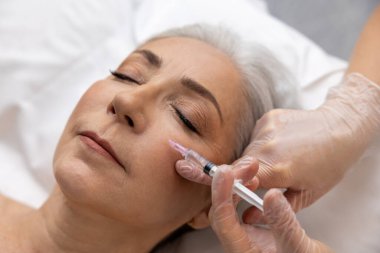 Yaş karşıtı prosedürler. Kadın göz bölgesine kırışıklık önleyici enjeksiyon yaptırıyor.