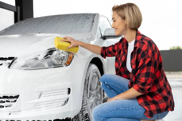 洗车的事穿着格子衬衫的金发女人洗一辆白色的车 — 图库照片