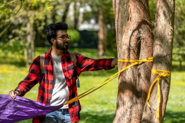 Genç Hintli adam parktaki ağaca hamak yapıyor.