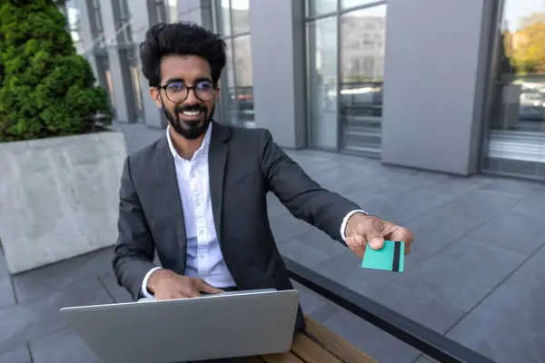 Young businessman working on laptop and holding access card in hand