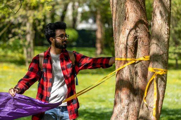 Genç Hintli adam parktaki ağaca hamak yapıyor.