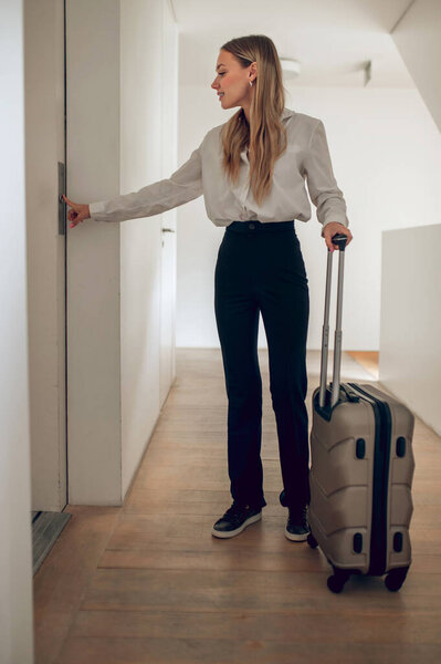 В отеле. Девушка с чемоданом, стоящим возле двери в отеле.