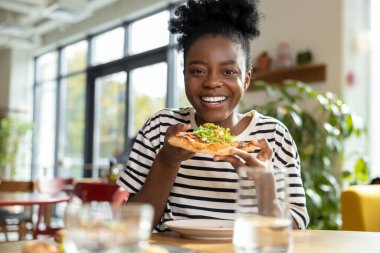 Elinde bir dilim pizza olan Afro-Amerikan kadın.