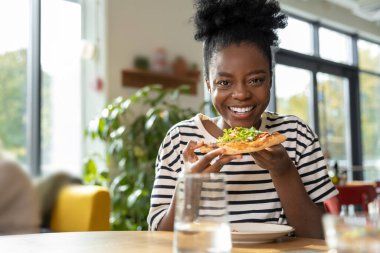 Elinde bir dilim pizza olan Afro-Amerikan kadın.