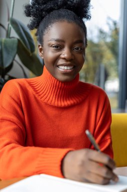 Gülümseyen Afrikalı Amerikalı kadın notlar alıyor ve kendini iyi hissediyor.